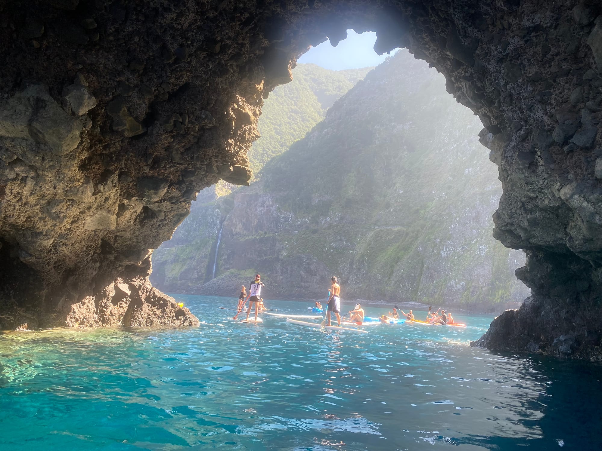 Paddleboarders and kayakers beneath a lava-rock sea arch on Seixal's coast