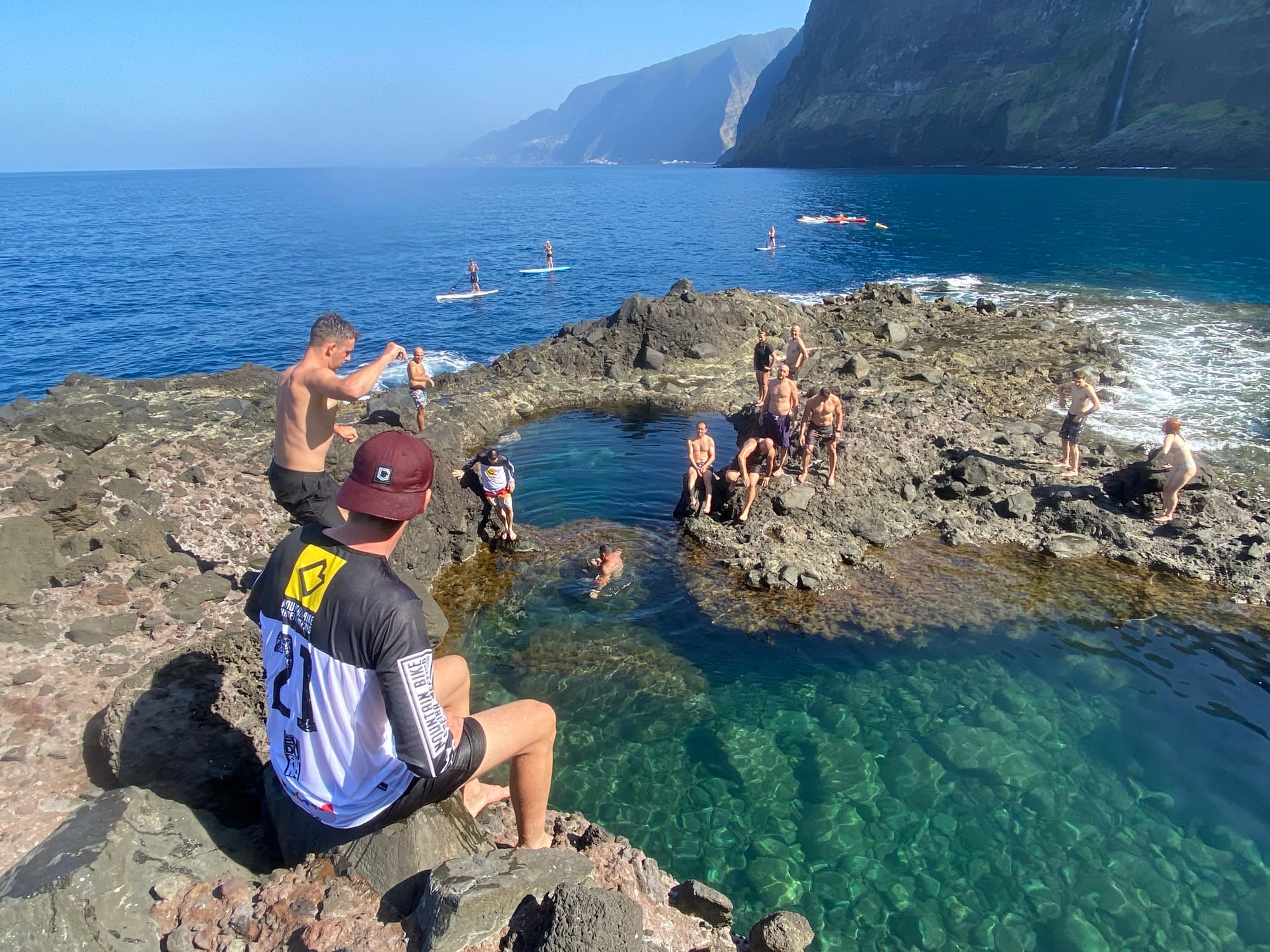 Riders at a natural lava-rock pool on Seixal's coast, paddleboarders out on the sea