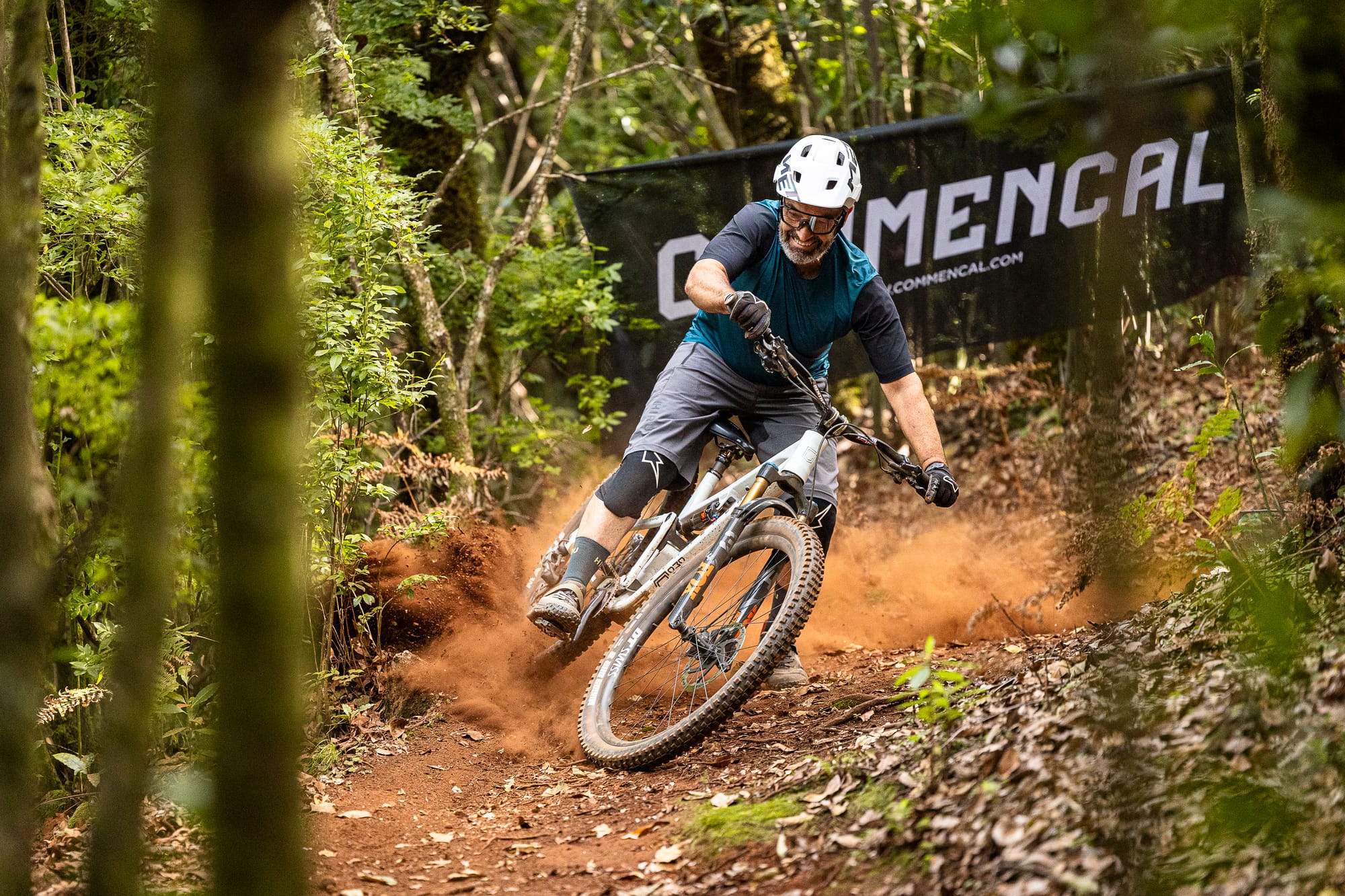 Rider railing a dusty corner beneath a Commençal banner in the forest